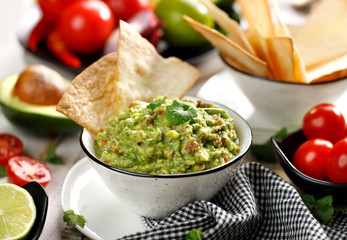 Guacamole is a traditional Mexican dip made of avocado, onion, tomatoes, coriander, chilli peppers, lime and salt with the addition of tortilla in a ceramic bowl.  Healthy vegetarian dish 