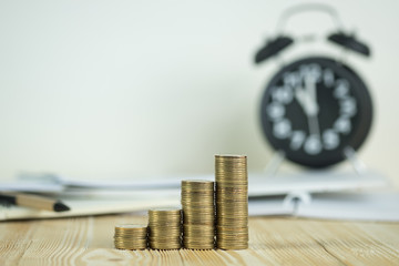 Steps of coins stack with vintage alarm clock and pen, notebook paper on wooden working table with copy space for text, financial and business planning concept..
