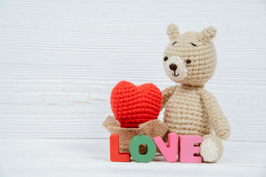 Sweet teddy bear doll  with Love text and red knitting heart on white wooden background and copy space for add text and picture, love and valentine day concept.
