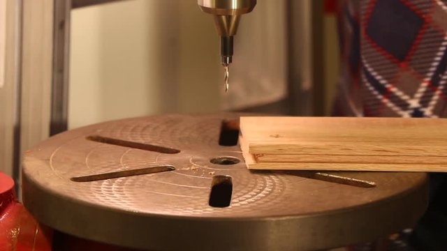 Close up shot of a man using a drill press to drill a hole in a piece of wood