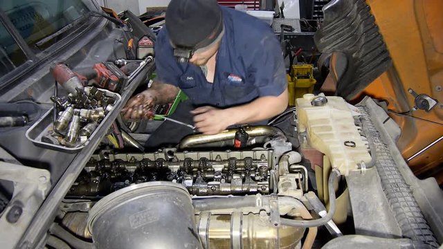 Mechanic working on semi diesel truck engine in repair shop garage