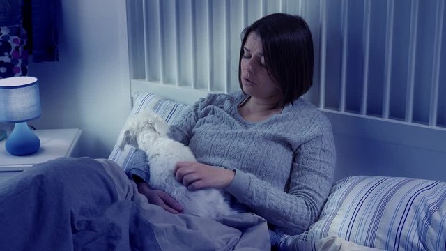 Sad woman sitting in bed at night caressing dog
