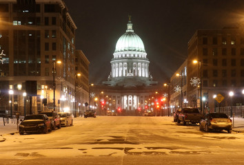 Beautiful snowy winter night. Madison, the capitol of Wisconsin downtown street view with parked cars and Wisconsin state capitol building glowing in the blizzard night. Wisconsin state, Midwest USA.