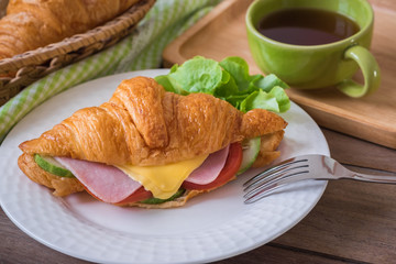 Croissant with ham, cheese on white plate and coffee cup.