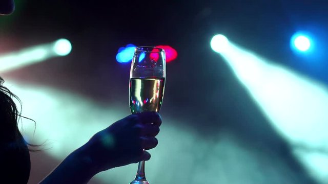 Girl holding a glass of champagne on the background of bright colored spotlights. Close-up of a glass of champagne in the hands of the girls at the party.