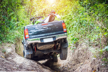 4 wheel drive with a motorcycle on the tailgate is climbing on a difficult off-road in mountain forests in Thailand. © ETAP