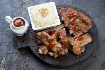 Black wooden serving board with baked pork ribs, mashed potato and sauce, studio shot