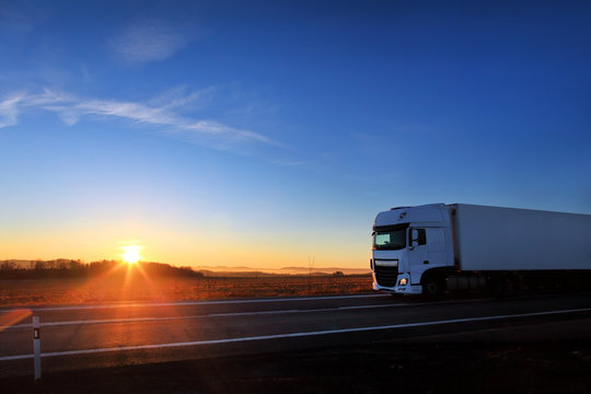 Truck driving through autumn landscape at sunset