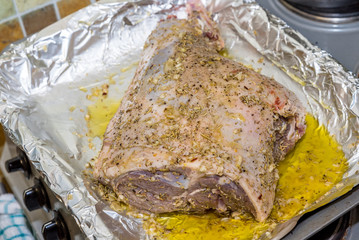 Closeup raw lamb leg joint on roasting tin foil with ingredients ready for roasting
