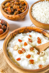 Rice milk porridge with nuts and raisins in wooden bowls on a white wooden table.