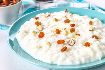 Rice milk porridge with nuts and raisins in a blue dish on a white wooden table.