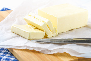 A bar of butter on a wooden board with a knife, on a white table. Ingredients for cooking.
