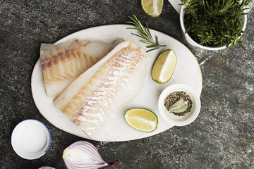 Cod fillet of cod fish with fresh vegetables: sweet pepper, rosemary, sweet red onion, ground pepper on a white cutting board on a grunge gray background. Top View. Copy space
