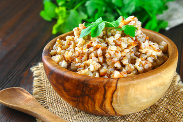 Boiled buckwheat in a bowl with pieces of chicken meat and cilantro on a brown wooden table.