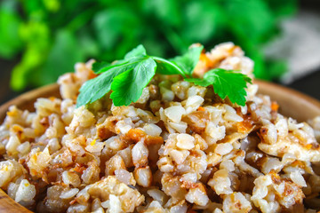 Boiled buckwheat in a bowl with pieces of chicken meat and cilantro on a brown wooden table.