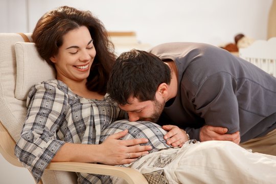 Pregnant woman relaxing, husband kissing belly