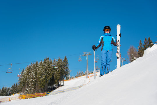 Full length portrait of a happy female skier standing with her skis on the slope, smiling to the camera, wearing blue ski suit, mask and black helmet copyspace ski-lift winter resort Bukovel