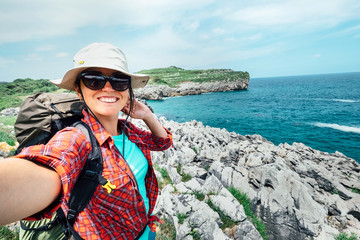 Happy woman backpacker traveler take a selfie photo on amazing ocean coast. Asturias. Spain