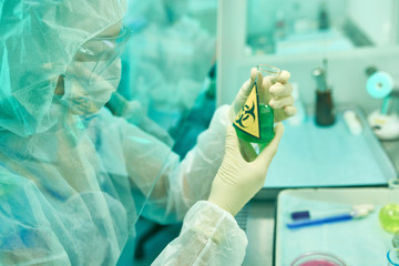 Side view portrait of unrecognizable female scientist wearing protective suit and mask working with...