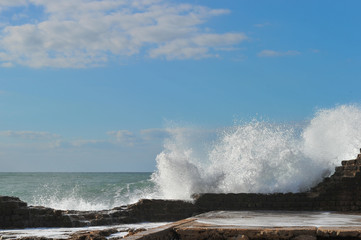 Waves breaking over coastal cliffs and breakwater during the storm, making a big splash of seawater