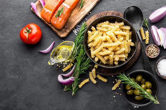 Pasta, salmon fish and ingredients for cooking on black background, top view. Italian food