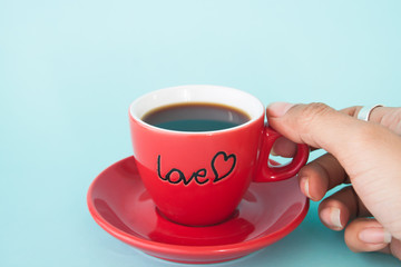 Woman's hand holding red cup of coffee with LOVE on pastel color, Love and Valentine's Day concept