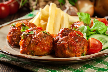 Roasted meatballs in tomato sauce with french fries and salad