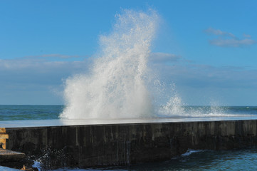 Waves breaking over coastal cliffs and breakwater during the storm, making a big splash of seawater