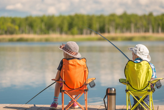 children with fishing rods sit on a wooden pier and fish at the lake