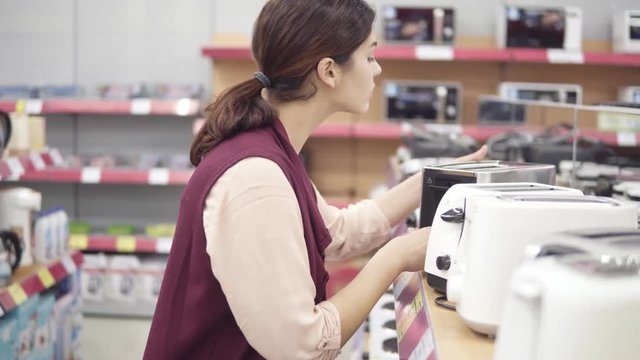 Young female costumer choosing new toster in appliance store. Looking for kitchenware.