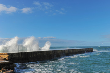 Waves breaking over coastal cliffs and breakwater during the storm, making a big splash of seawater