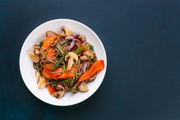 Delicious fresh pad thai noodles with mushrooms and vegetable slices on dark background, flat lay...