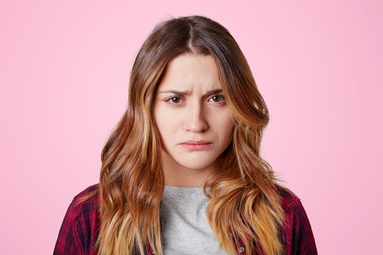 Attractive Offended Female With Dissatisfied Expression, Curves Lips, Going To Cry As Being Abused By Close Person, Didn`t Expect Such Bad Attitude Towards Her, Isolated Over Pink Background