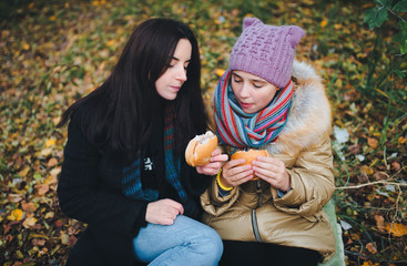 Mother and daughter eating hamburgers at a picnic in the park. Autumn