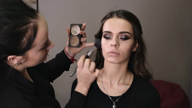 make-up artist applies powder with a professional brush on the face of the girl