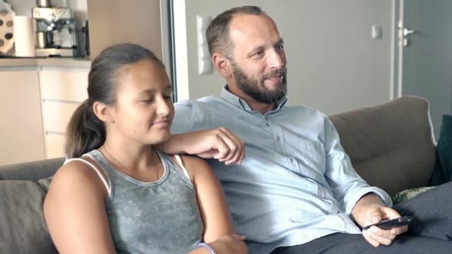 Happy father with daughter watching TV sitting on sofa at home
