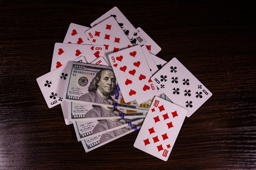 Playing cards and one hundred dollar bills on a dark wooden table