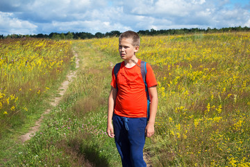 Thoughtful little boy the traveler stands on a beautiful summer meadow, against a blue sky