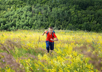 Fototapeta na wymiar The boy is a tourist in a bright T-shirt, runs along a beautiful flowering meadow