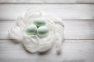 Fototapeta na wymiar Three green easter eggs and white feathers on wooden table