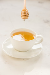 Honey pouring from stick into a cup with tea
