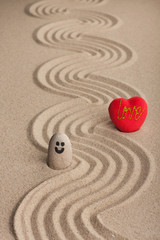 Fototapeta na wymiar Stone smiley and a red heart stand on a zigzag from the sand.