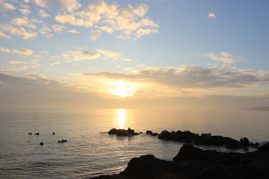 idyllischer Sonnenaufgang mit blauem Himmel und Wolken an einer Buhne an der Ostsee
