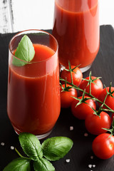 Tomato juice in a glass with a cherry and basil on a light background
