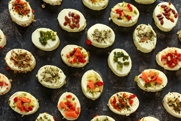Creamy cheese bites garnished with pesto, red peppers, herbs, garlic, tomato, olives, shallots, onions and carrots. Party Finger food.