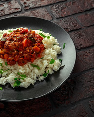 Homemade beef mince and vegetable casserole served with rice on black plate.