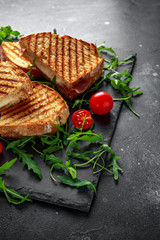Grilled Bacon, cheese sandwich and served on stone platter with arugula and tomatoes