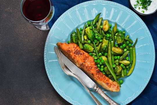 Baked salmon steak with asparagus, Brussels sprouts and green peas on a concrete background with a glass of wine.