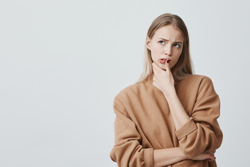 Indoor shot of thoughtful beautiful woman with long blonde hair, looks upwards with pensive...