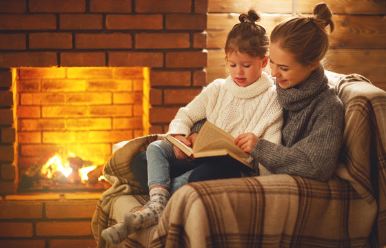 happy family mother and child daughter read book on winter evening near fireplace